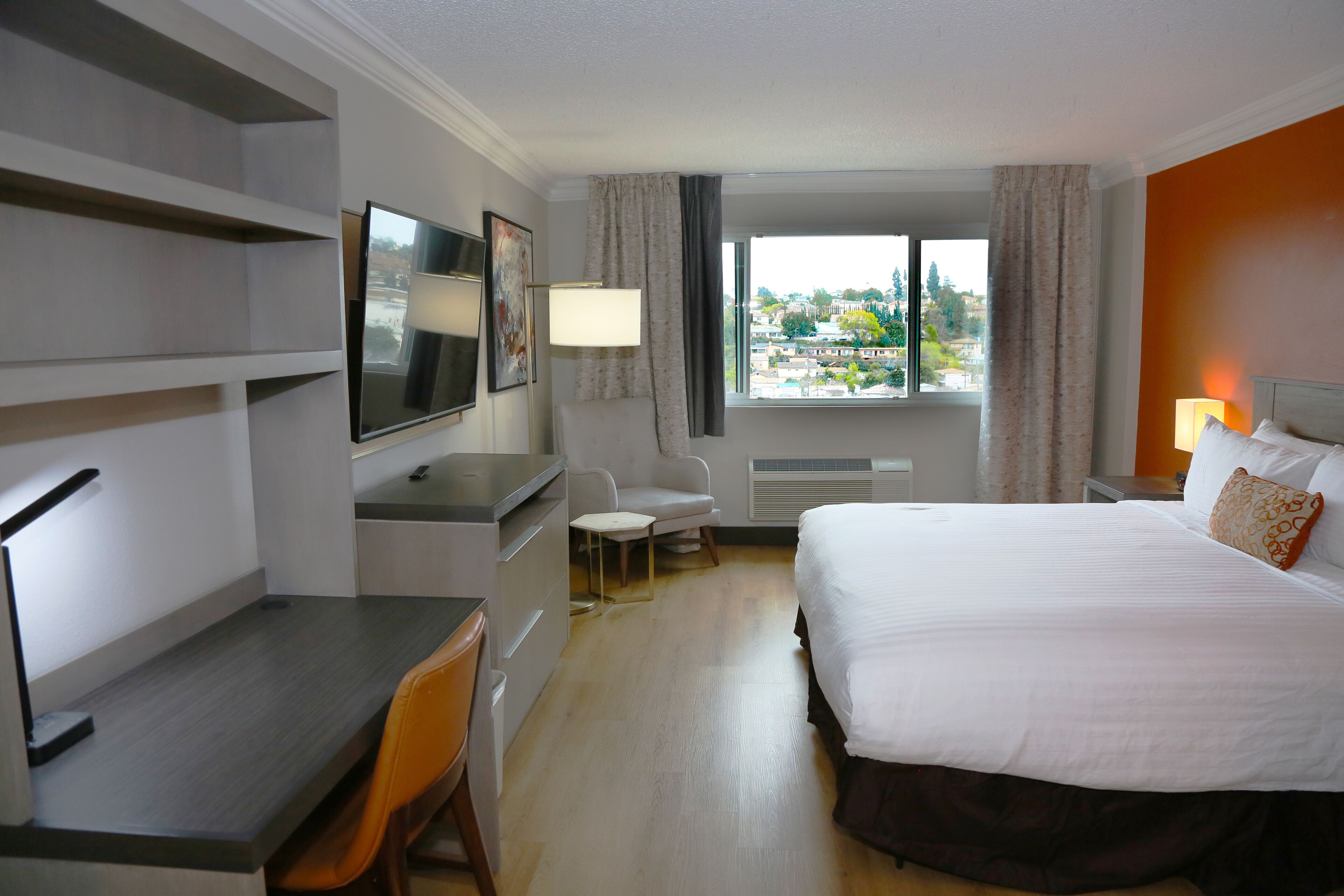 Habitación de hotel con cama, escritorio, silla, televisión y ventana con vistas a edificios.