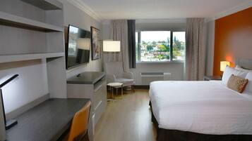 Habitación de hotel con cama, escritorio, silla, televisión y ventana con vistas a edificios.