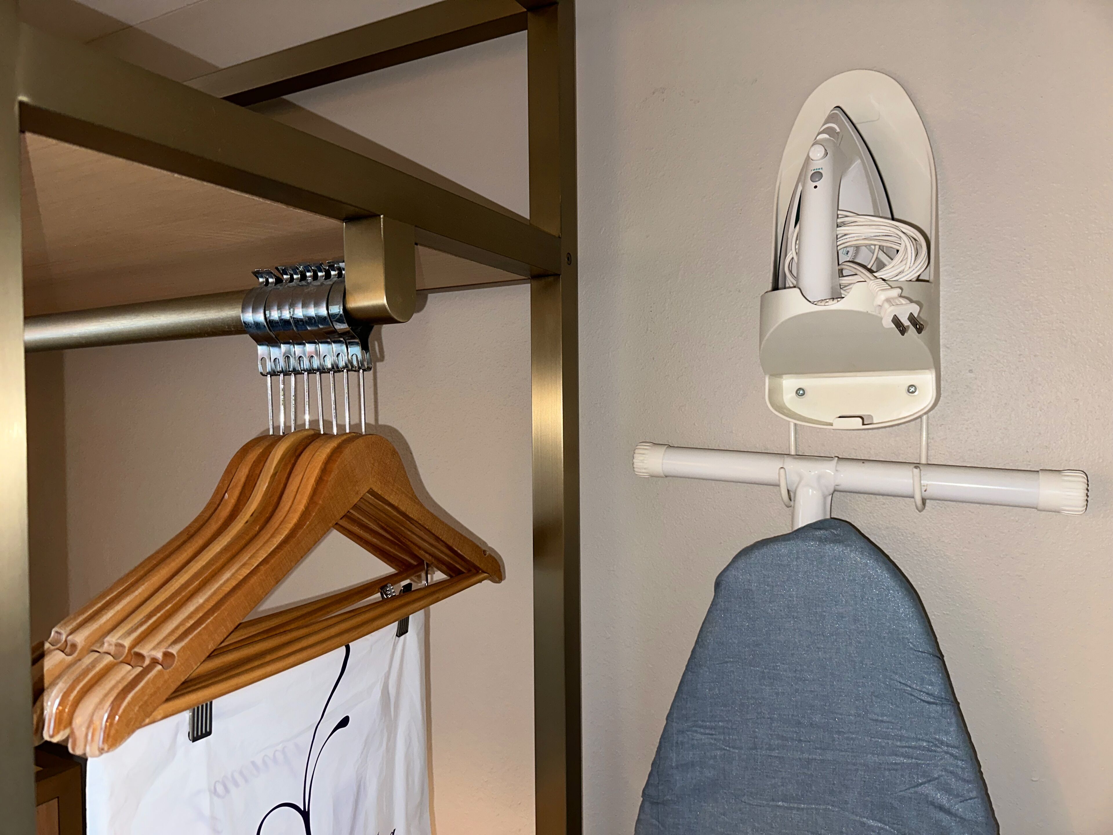 Un perchero de madera y una camisa blanca colgados en una barra metálica en una habitación con pared y techo blancos.