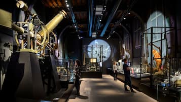 An indoor exhibition space with a large telescope, glass display cases, and a projection screen.