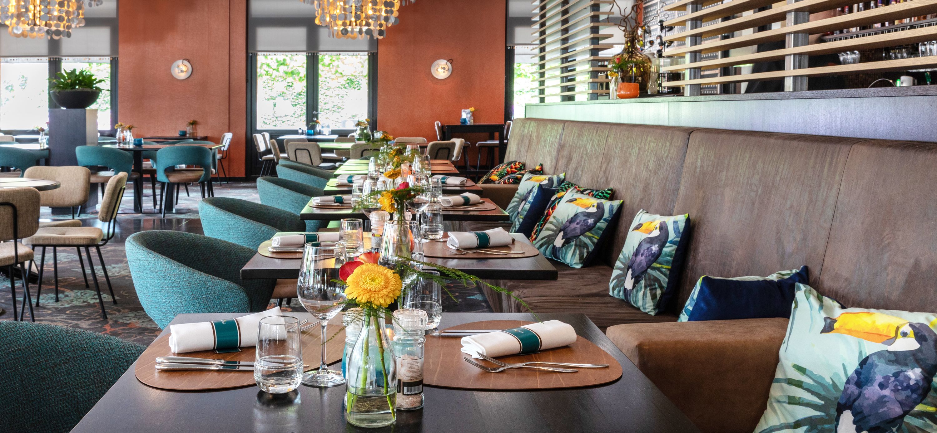 Een restaurant met meerdere eettafels gedekt voor gasten, met een modern interieur met houten details en teal stoelen.
