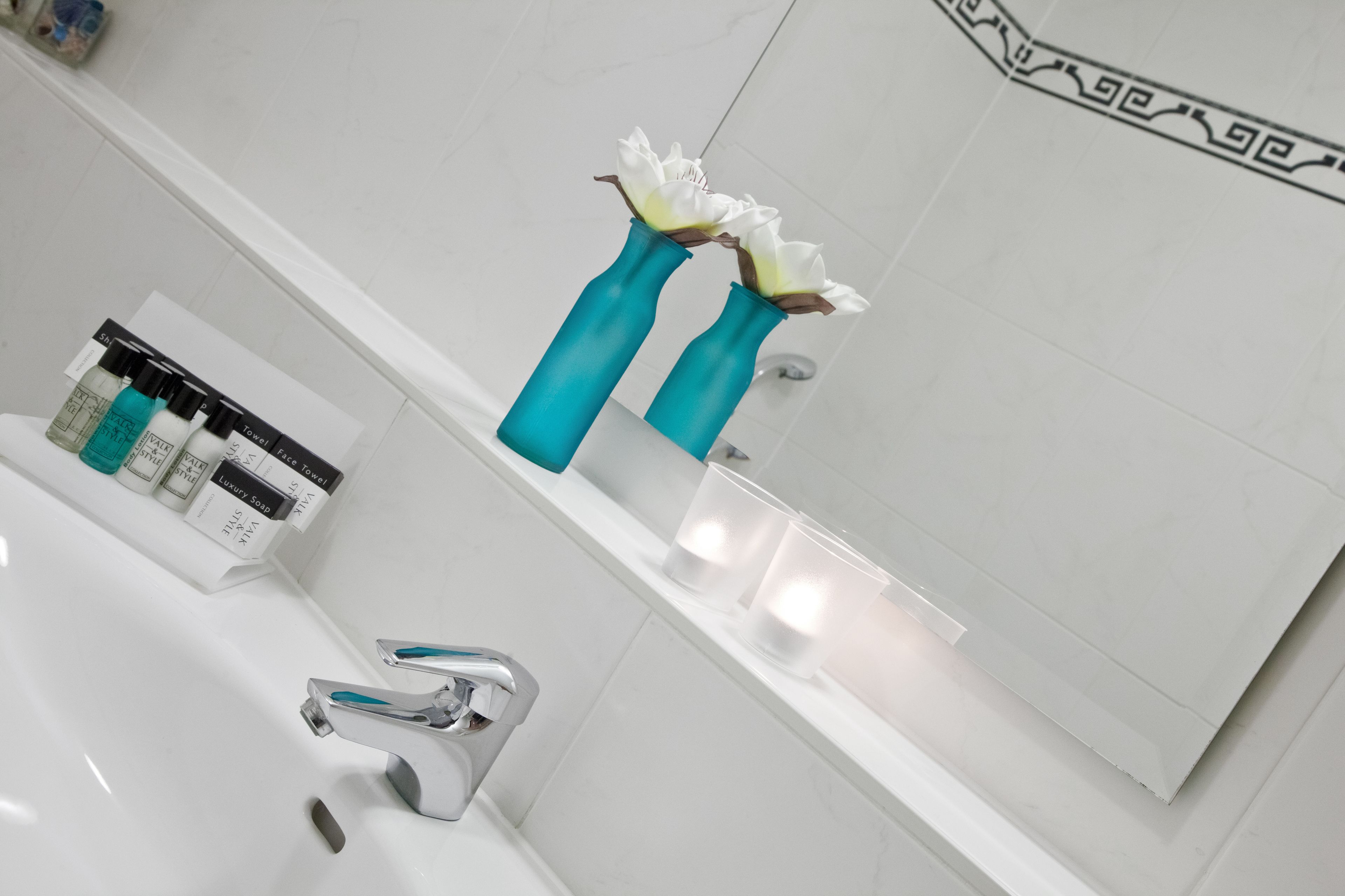 A modern bathroom with a white sink, two teal vases with white flowers, and a mirror with a decorative border.