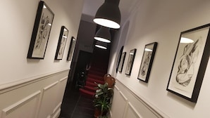 A hallway with framed artwork on the walls, a staircase with red steps, and a potted plant. - Exhibition Court Hotel 4 (London)