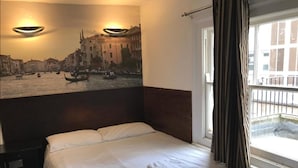 A hotel room with a bed, a painting of a cityscape, and a window with curtains. - Exhibition Court Hotel 4 (London)