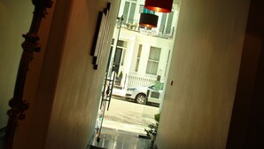 A narrow hallway with a glass floor, leading to a balcony with a view of a street and parked cars. - Exhibition Court Hotel 4 (London)