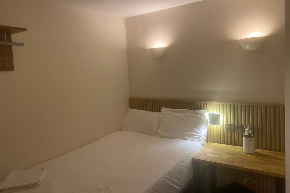 Een hotelkamer met een bed, nachtkastje en wandlampen.