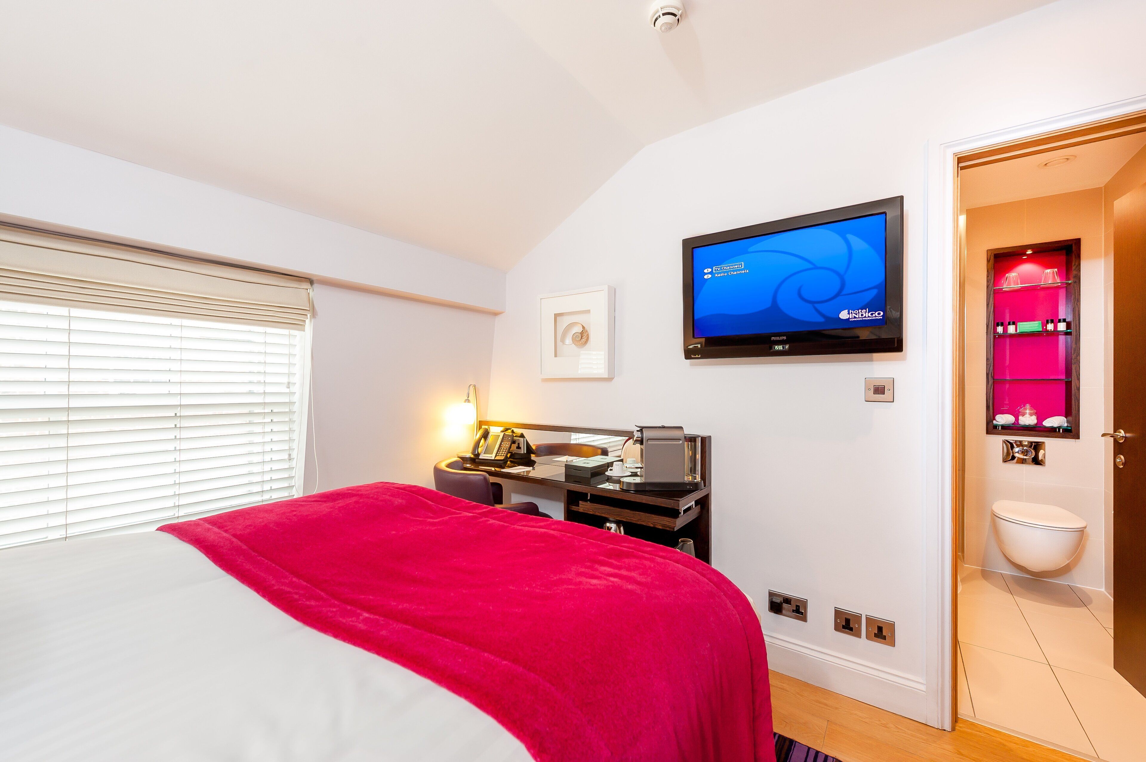 A hotel room with a bed, a desk with a computer, a television, and a bathroom with a toilet and sink.