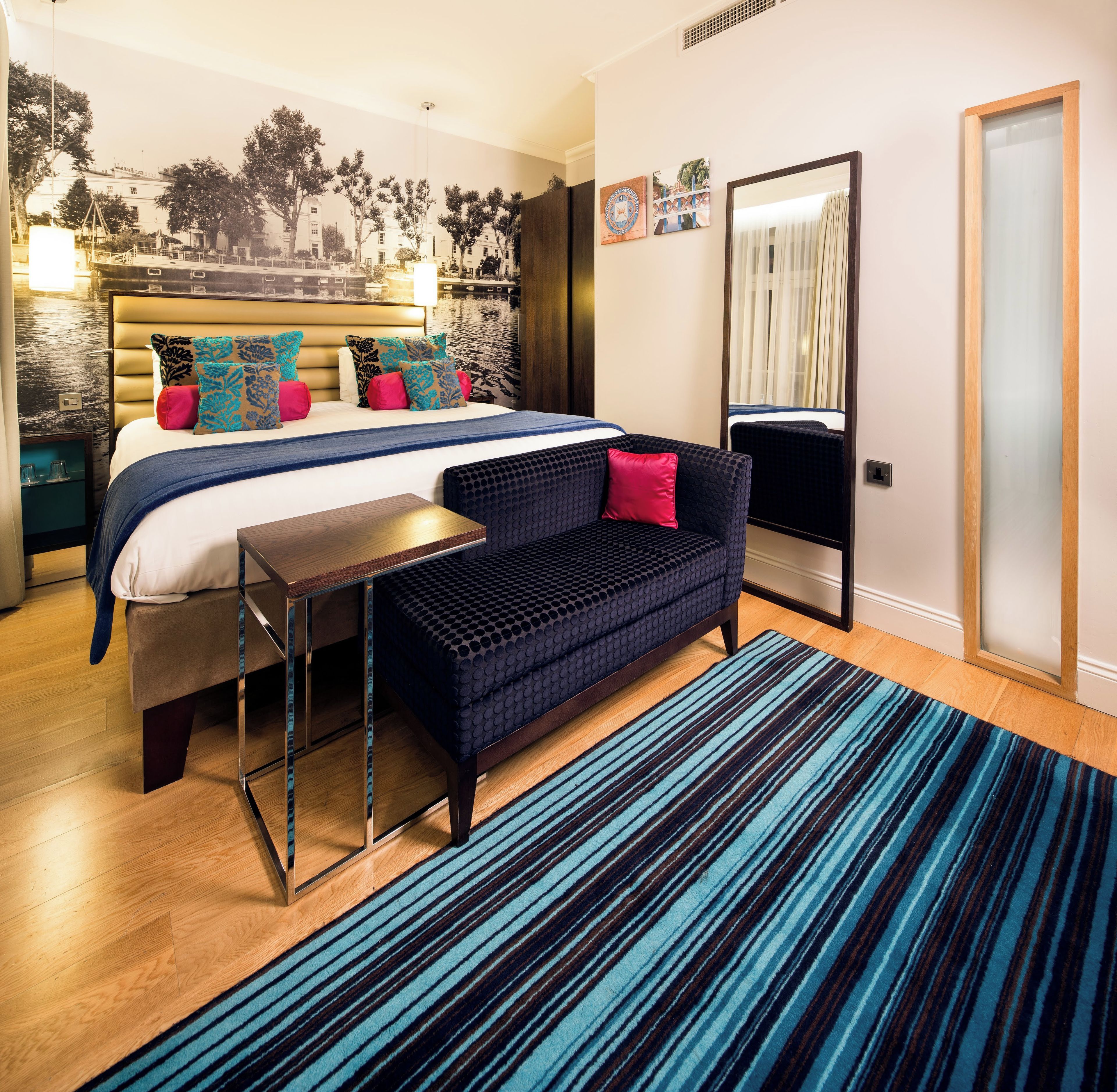 A modern hotel room with a large bed, a sofa, a small table, and a large mirror.