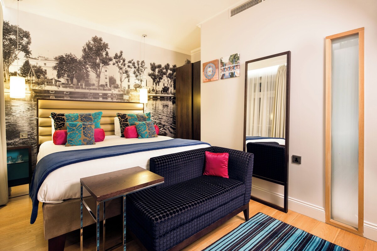 A modern hotel room with a large bed, a sofa, a small table, and a large mirror.