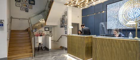 A reception area with a herringbone floor, a staircase, and a large wall-mounted screen displaying a logo.