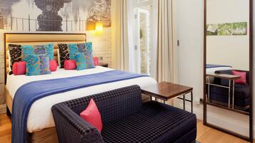 A hotel room with a bed, a sofa, a small table, a mirror, and a wall with a fountain and a statue.