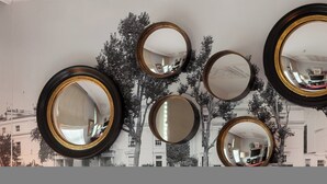 A wall with multiple round mirrors of varying sizes and frames, set against a backdrop of a monochrome building and tree mural.