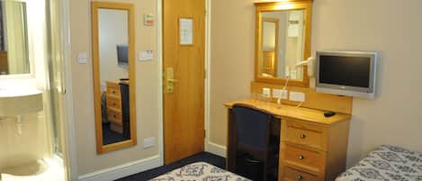 A hotel room with a wooden desk, a television, two beds with patterned bedding, a mirror, and a door leading to a bathroom.