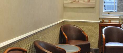 A room with a beige wall, a painting of vases, and three brown leather chairs with a small table.