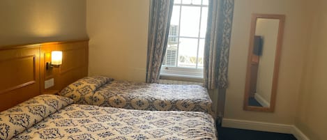 A hotel room with a large bed, a bedside lamp, a window with curtains, and a mirror on the wall.