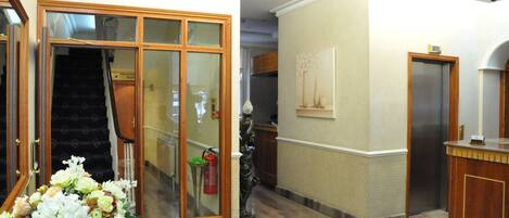 A hotel lobby with a staircase, a reception desk, and a fire extinguisher.