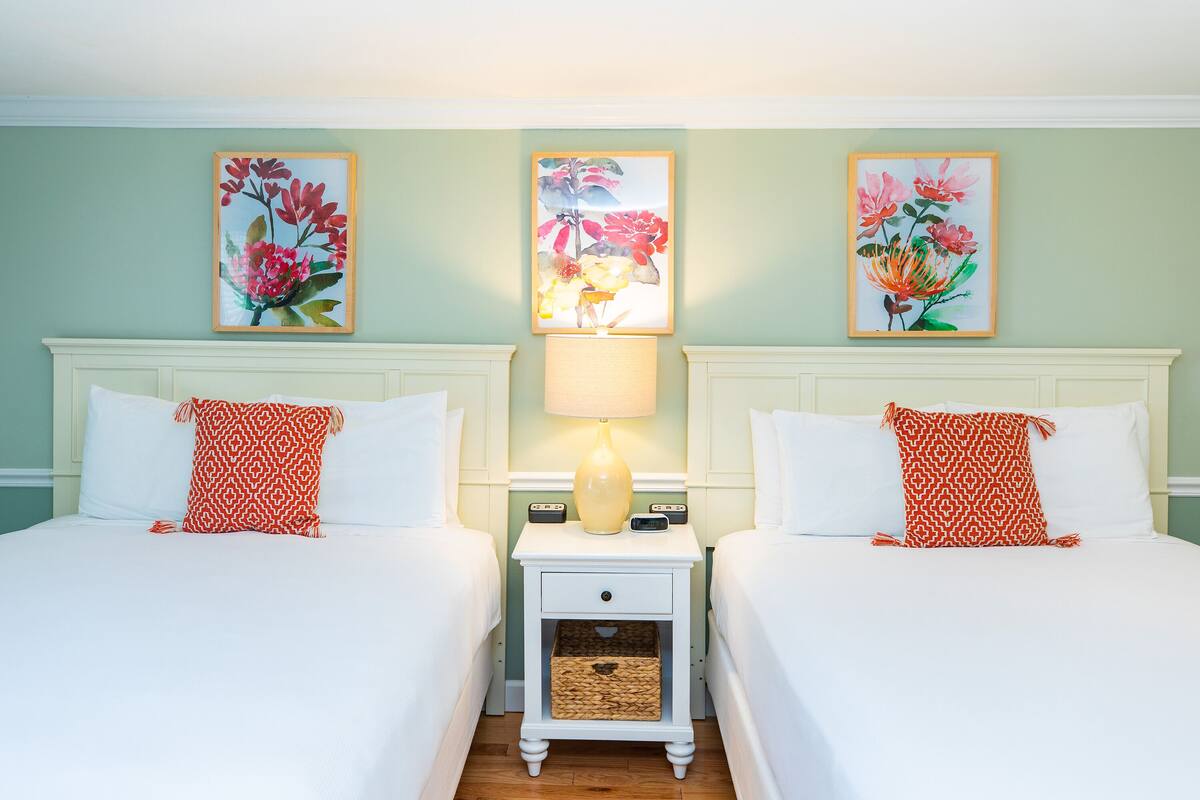 Une chambre d’hôtel avec deux lits, une table de chevet avec une lampe et des œuvres d’art florales accrochées aux murs.