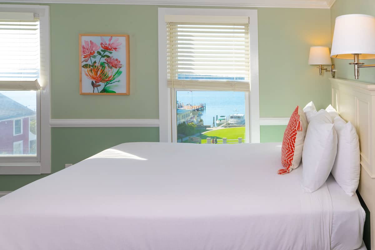 Un lit avec du linge de maison blanc, une vue sur l’eau et un tableau de fleurs accroché au mur.