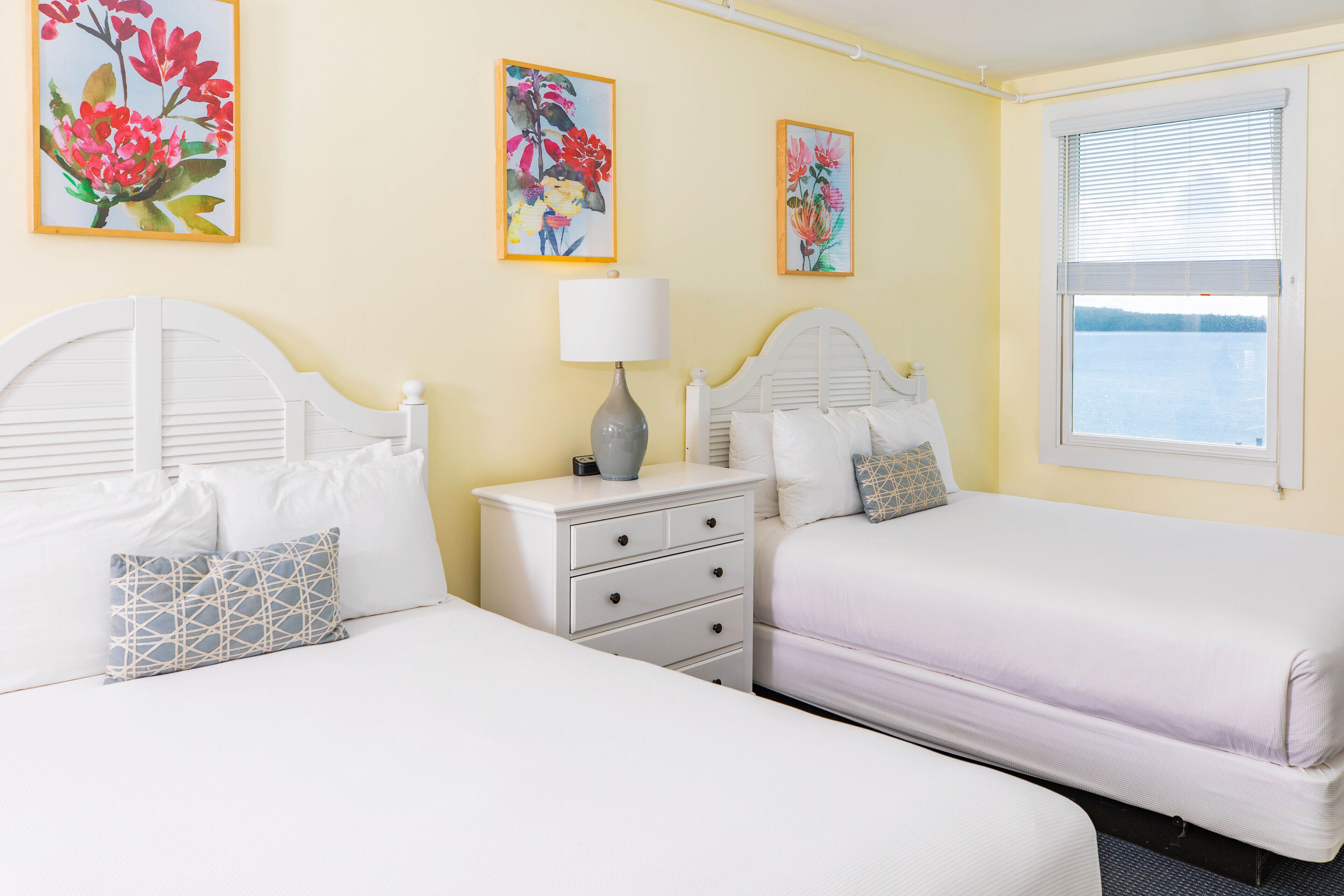 Une chambre d’hôtel avec deux lits, une table de chevet avec une lampe et des œuvres d’art florales accrochées aux murs.