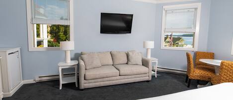 Ein Hotelzimmer mit grauem Sofa, einem kleinen Tisch, einem Stuhl, einem Bett und einem Fernseher an der Wand.