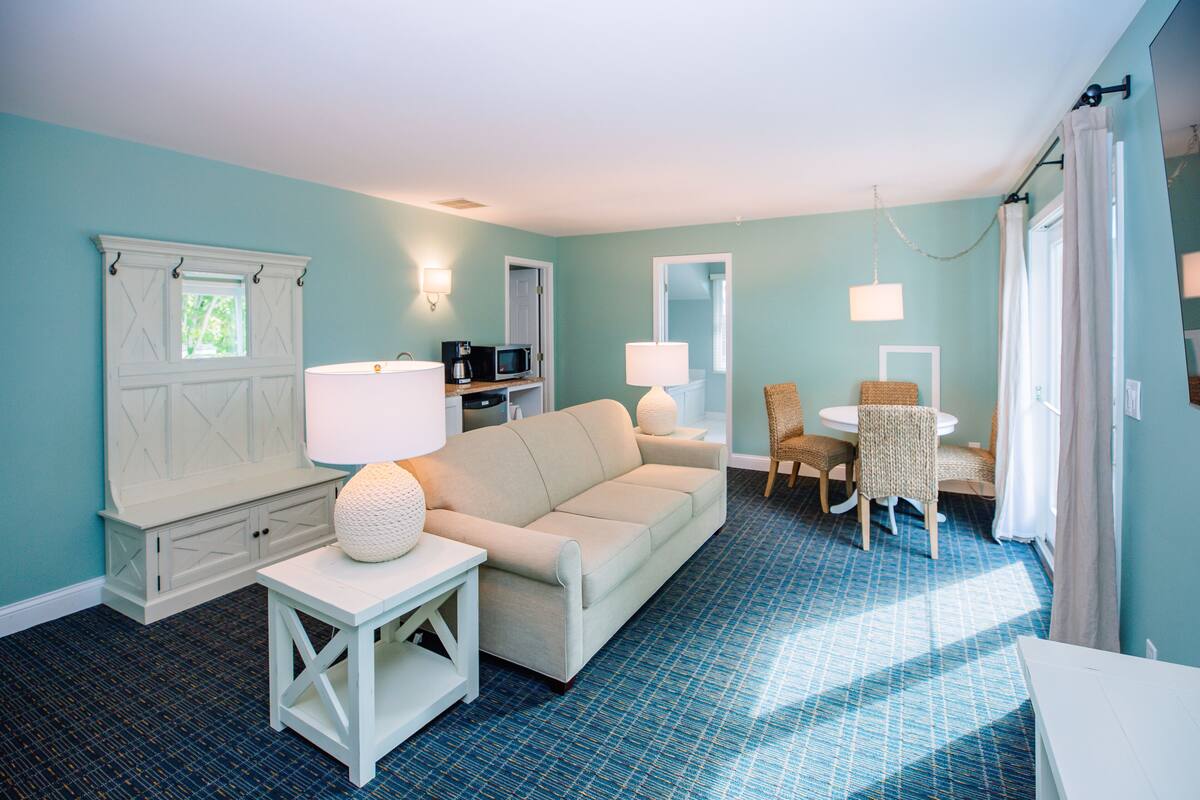 Un salon comprenant un canapé, une petite table, une lampe, un fauteuil, une table à manger et un coin cuisine avec un four à micro-ondes.