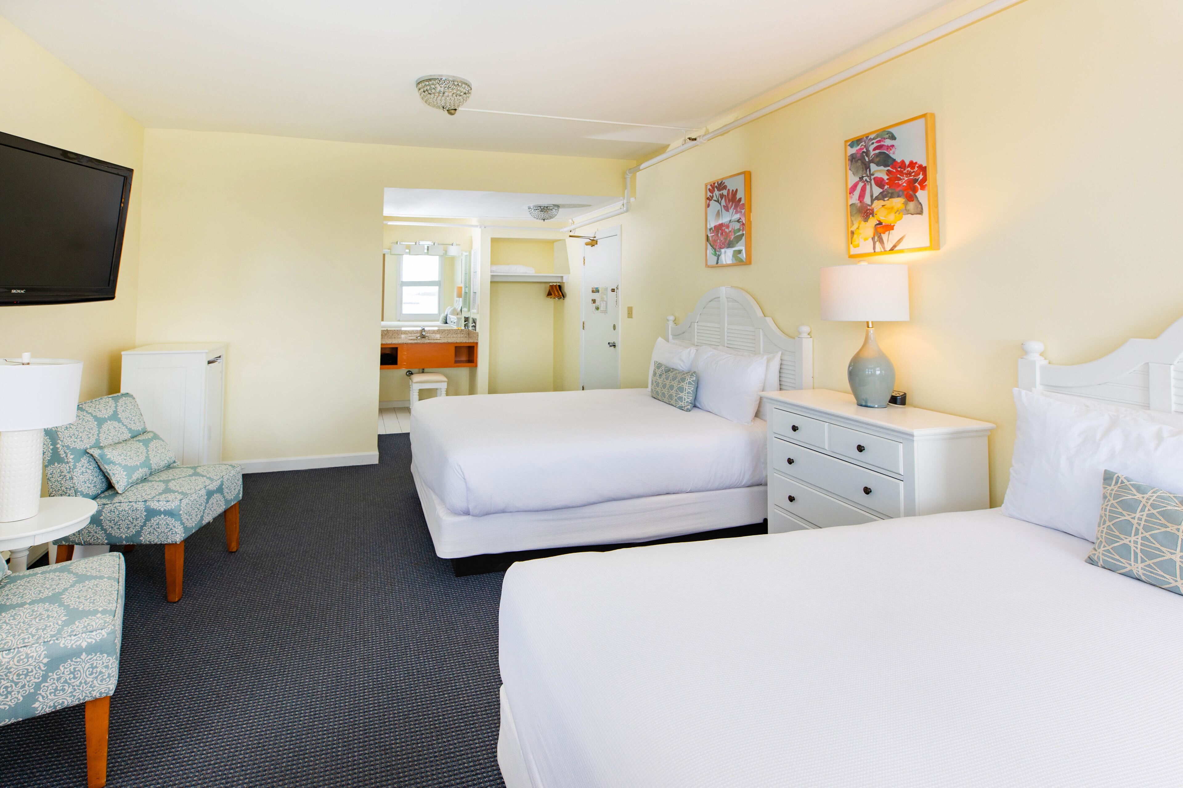 A hotel room with two beds, a TV, a desk, and a bathroom visible through an open door.