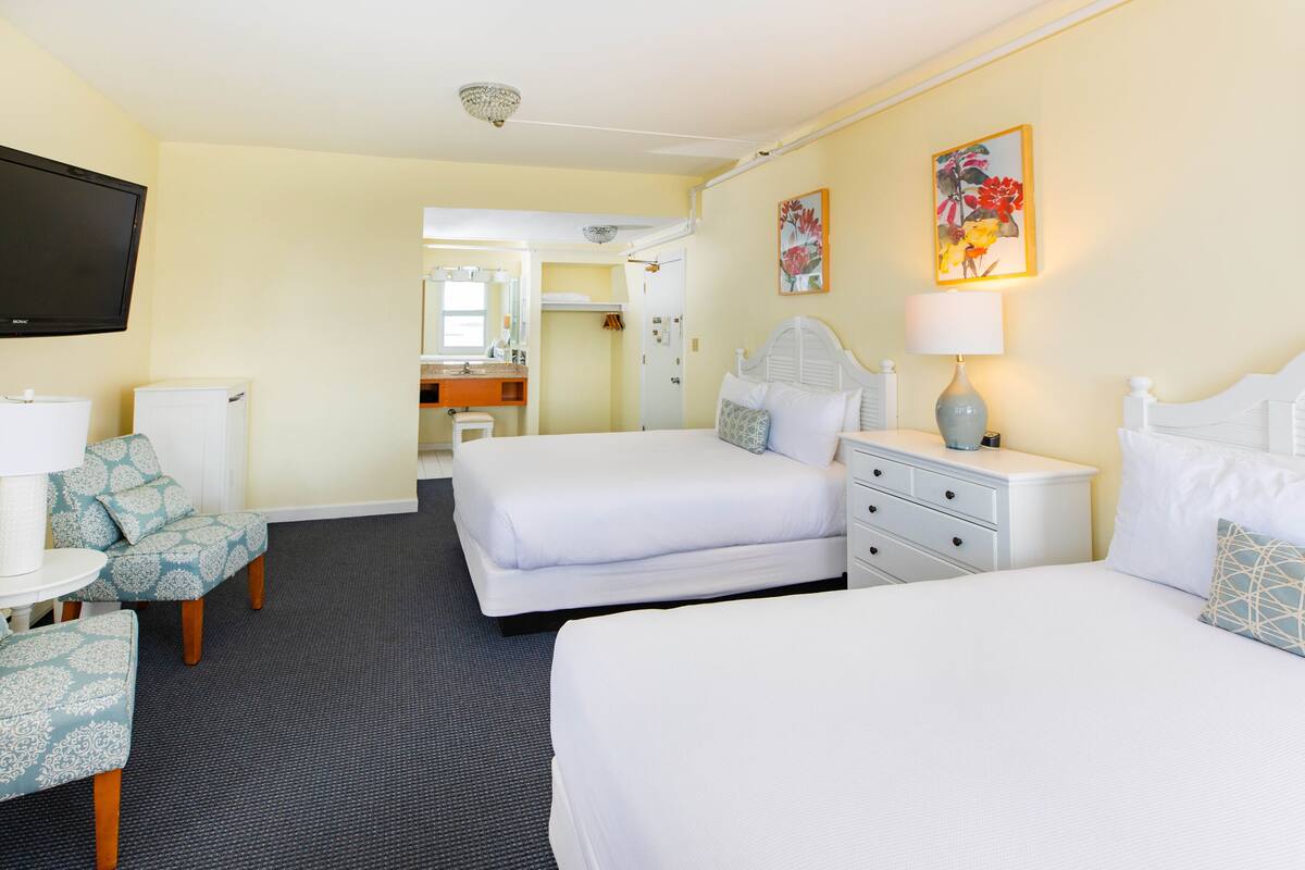 Une chambre d’hôtel avec deux lits, une télévision, un bureau et une salle de bain visible à travers une porte ouverte.