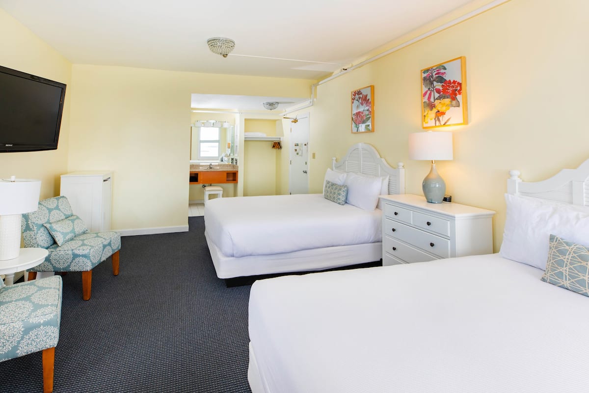 A hotel room with two beds, a TV, a desk, and a bathroom visible through an open door.