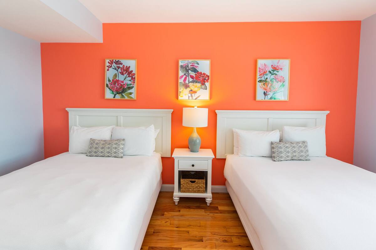 Une chambre d’hôtel avec deux lits, une table de chevet avec une lampe et des œuvres d’art florales accrochées aux murs.