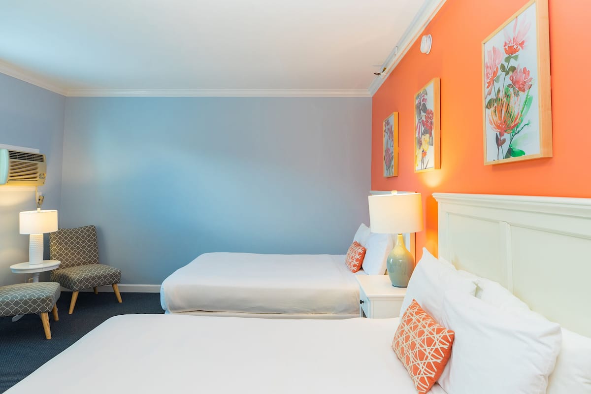 Une chambre d’hôtel avec deux lits, une chaise, une lampe et des œuvres d’art accrochées au mur.