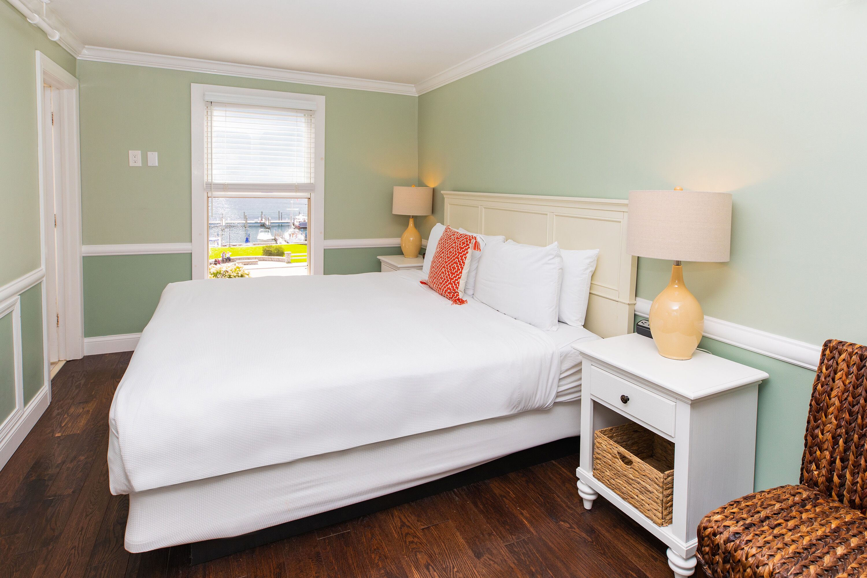 A bedroom with a large bed, two bedside tables, a chair, and a window with a view.
