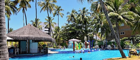 A swimming pool with palm trees, a thatched-roof hut, and a water play area.
