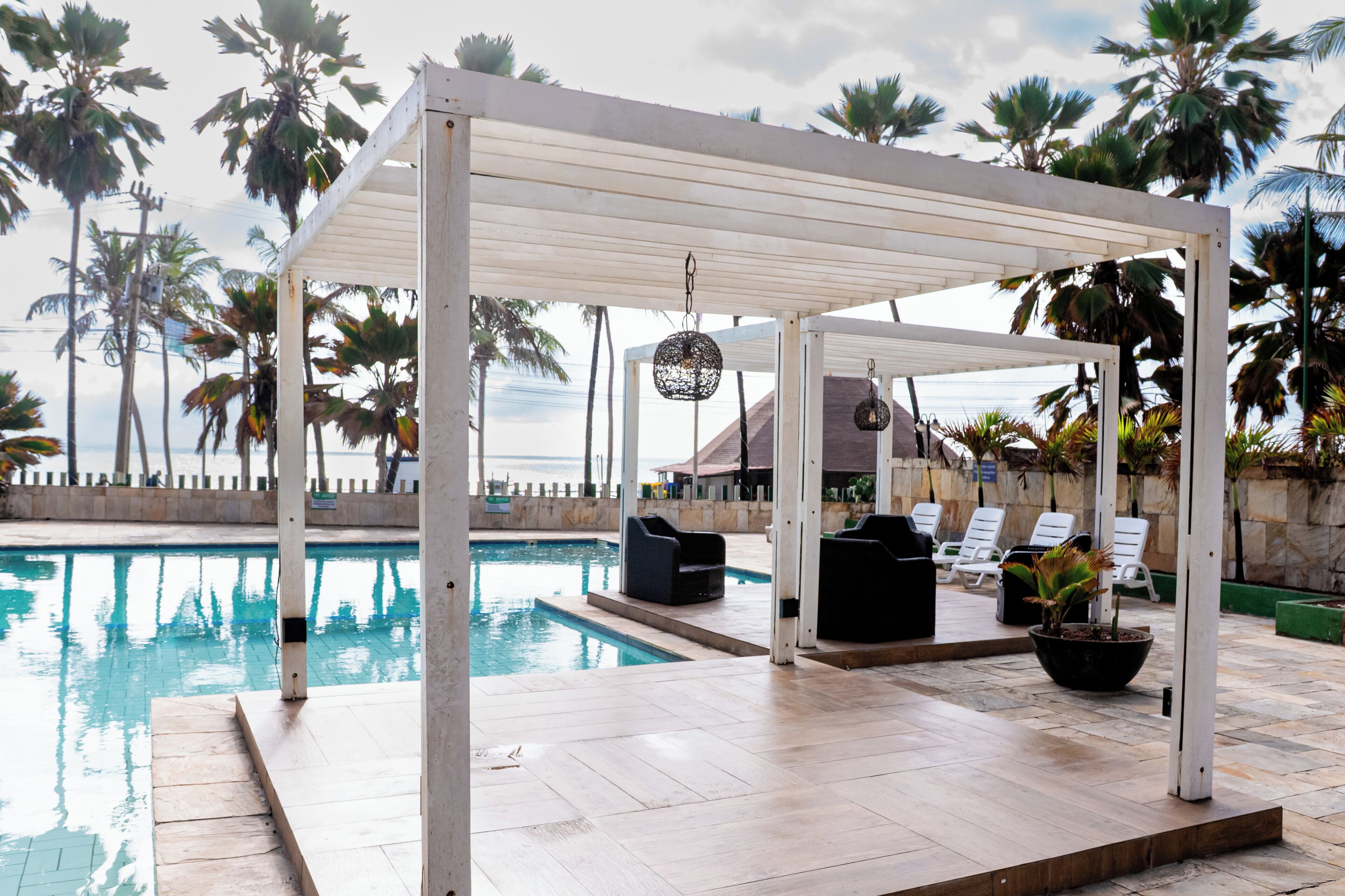 A poolside area with a covered seating area, lounge chairs, and a potted plant.