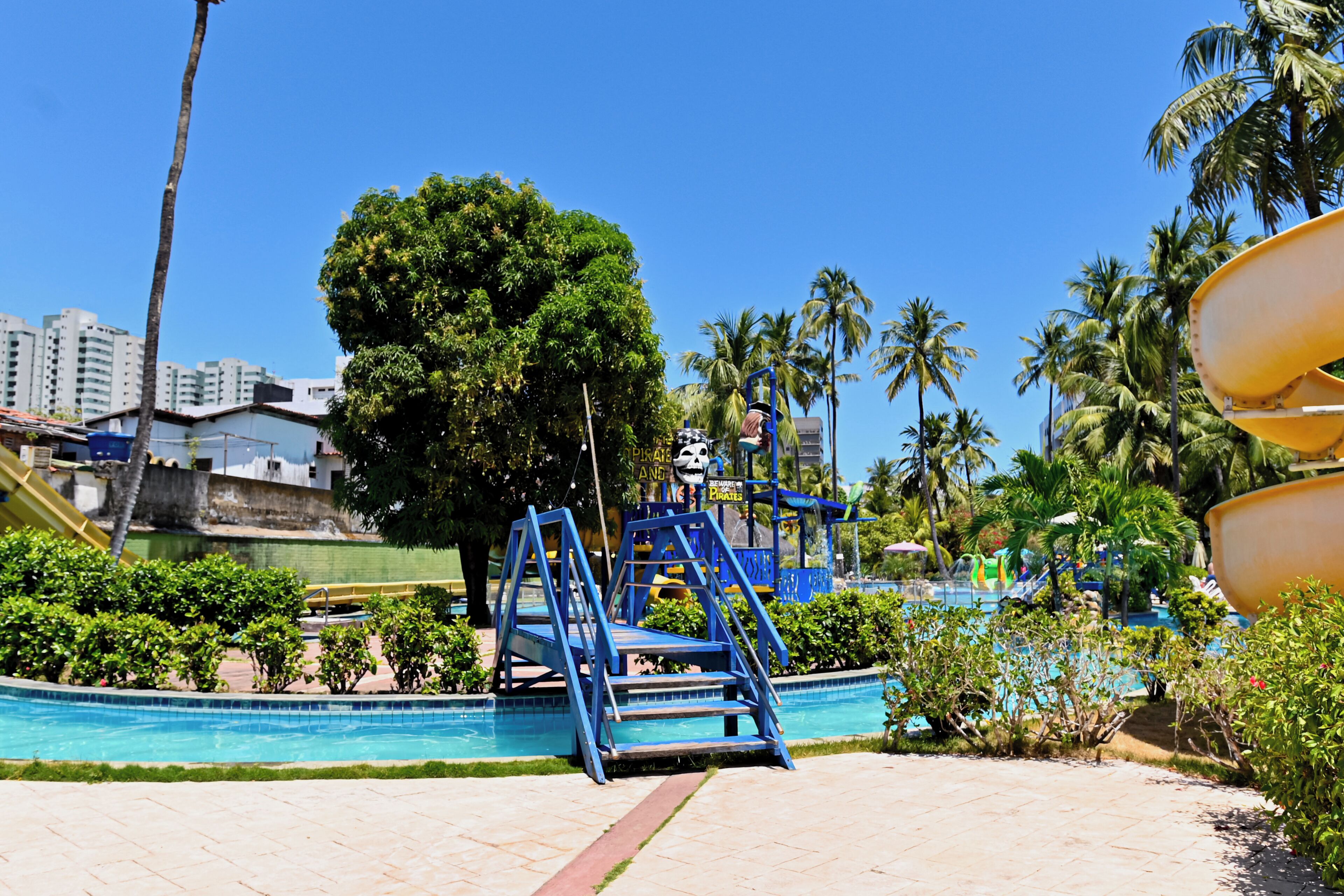 A swimming pool with blue steps and a lifeguard stand, surrounded by palm trees and buildings.