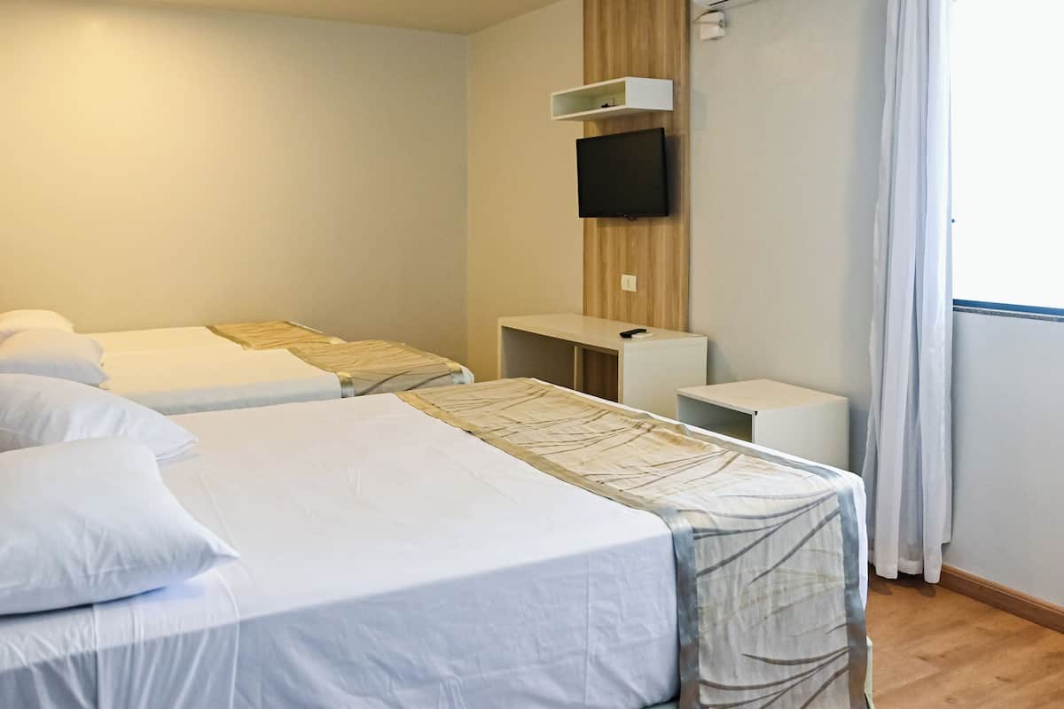 Habitación de hotel con dos camas, un televisor montado en la pared, un escritorio pequeño y una ventana con cortinas.