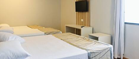 A hotel room with two beds, a TV mounted on the wall, a small desk, and a window with curtains.