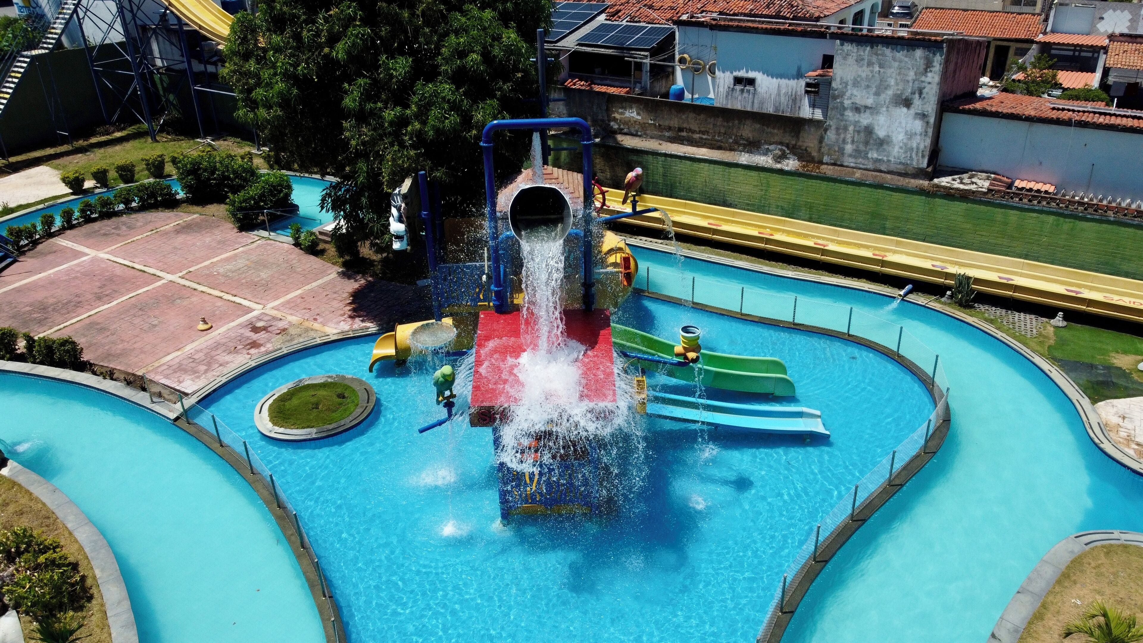 Een waterpark met een centrale glijbaan, meerdere zwembaden en veel groen eromheen.