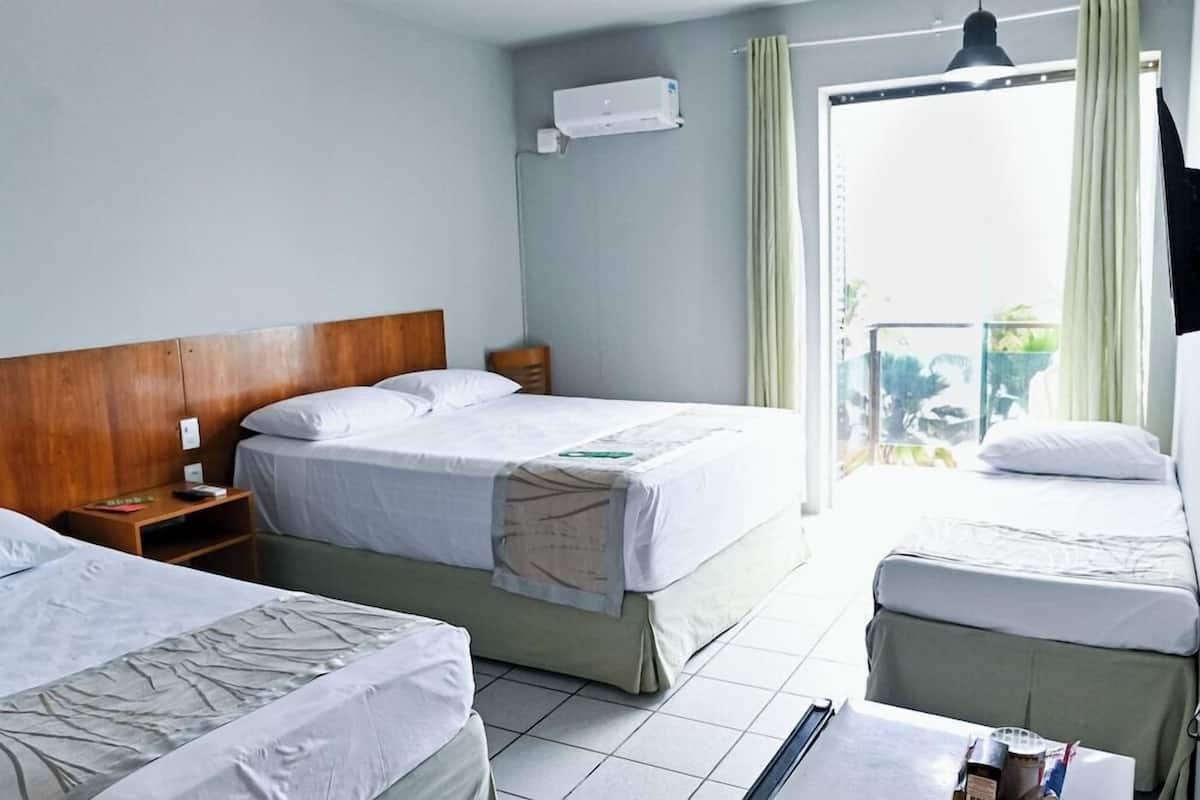 Habitación de hotel con dos camas, cabecera de madera, mesita de noche y unidad de aire acondicionado, con vista al exterior a través de una puerta de vidrio.
