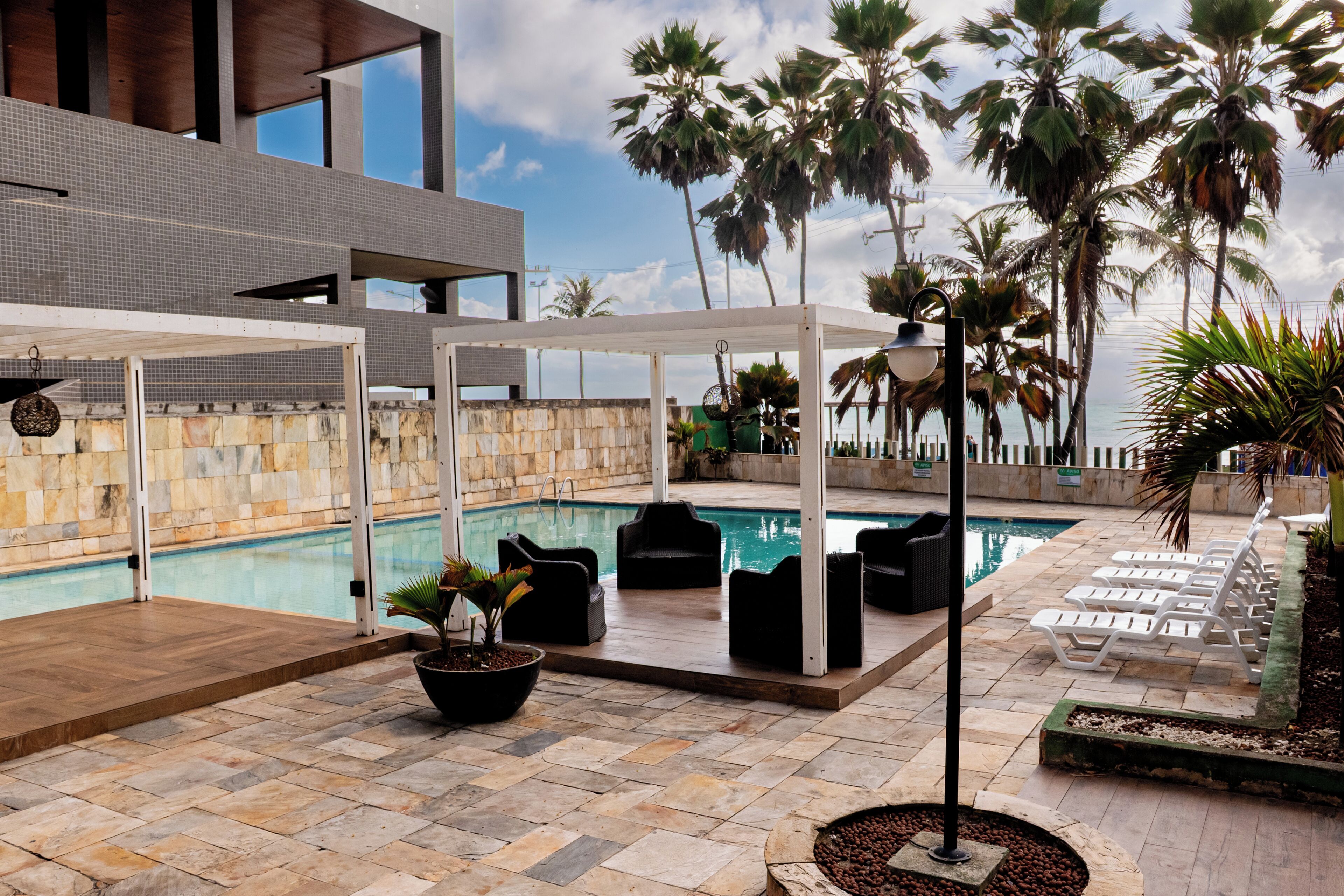 Zona de piscina con sillones de descanso, una pérgola y vistas al océano.