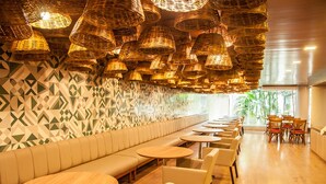 A restaurant with a long bench seating area, round tables, wicker ceiling lamps, and patterned wall tiles. - Matsubara Acqua Park Hotel (Maceió)