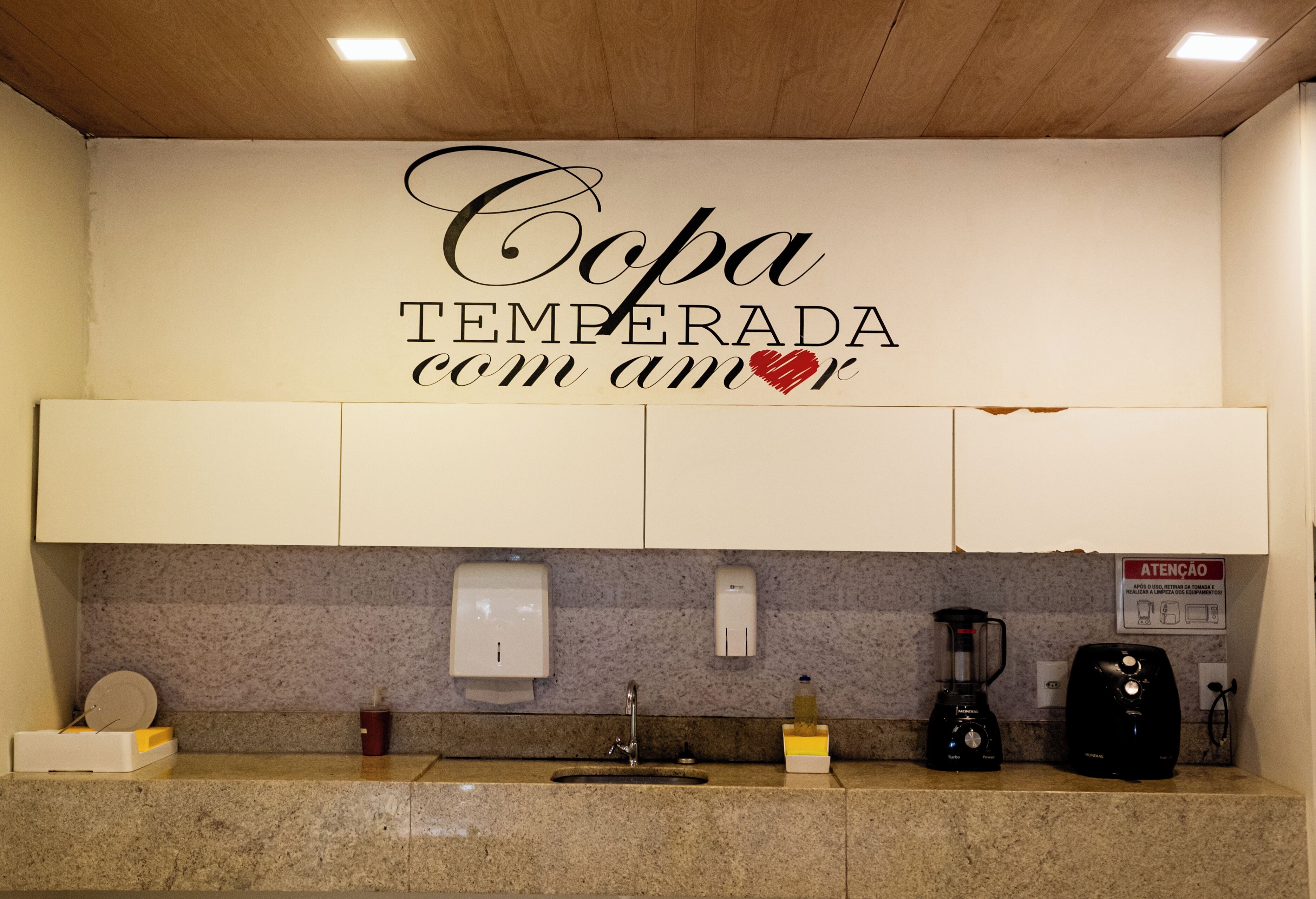 Cuina amb taulell de granit, un rentaplat, un preparador de cafè, un batllixer i un cartell a la paret que diu "Copa Temperada com amor".