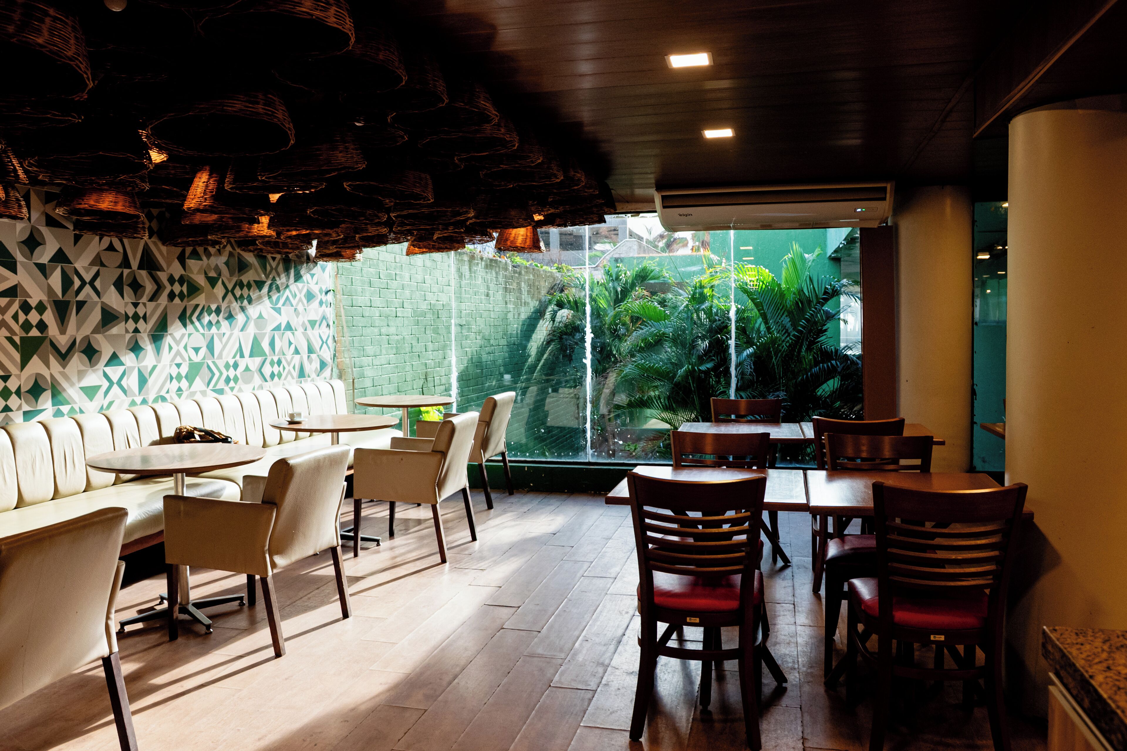 A restaurant with a modern interior, featuring a mix of seating options including a long counter and booths, with a view of greenery outside.