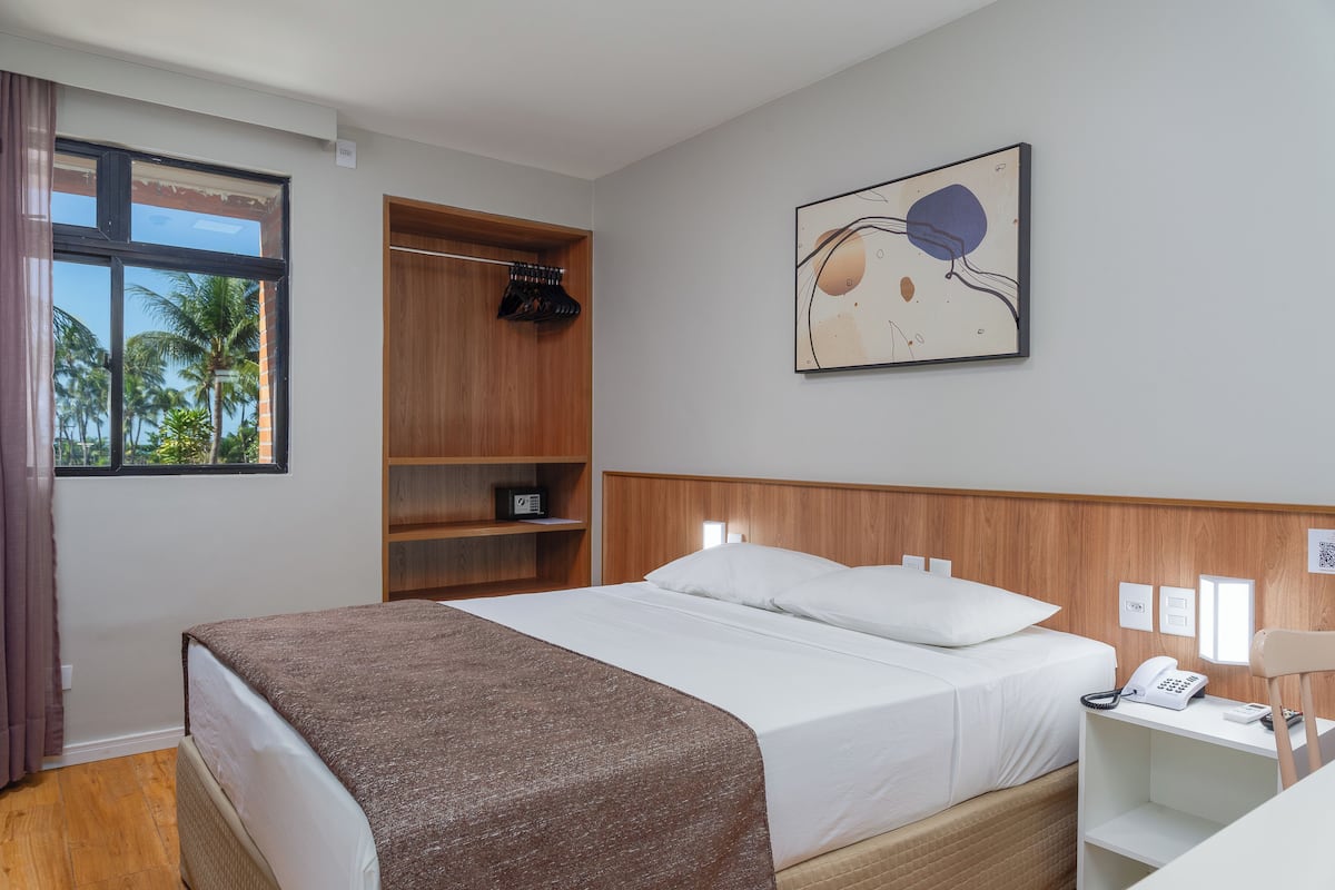Hotellihuone, jossa on sänky, puinen vaatekaappi, kirjoituspöytä puhelimineen ja taulu seinällä.