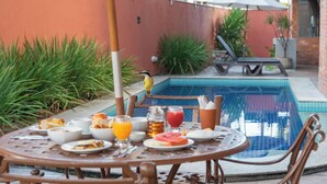 A round metal table with breakfast items, a bird on a chair, and a pool in the background. - Ritz Plazamar Hotel (Maceió)