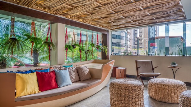 Ein stilvoller Lounge-Bereich mit einer gebogenen Couch, Korpusfußhocker und Blick auf Palmen durch große Fenster.