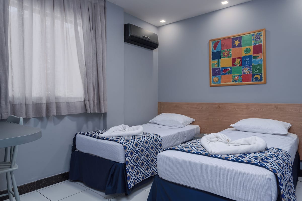 A hotel room with two beds, a small table, and a colorful artwork on the wall.