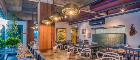 Un restaurante con mesas comunes largas, lámparas colgantes y una combinación de decoración de madera y metal.