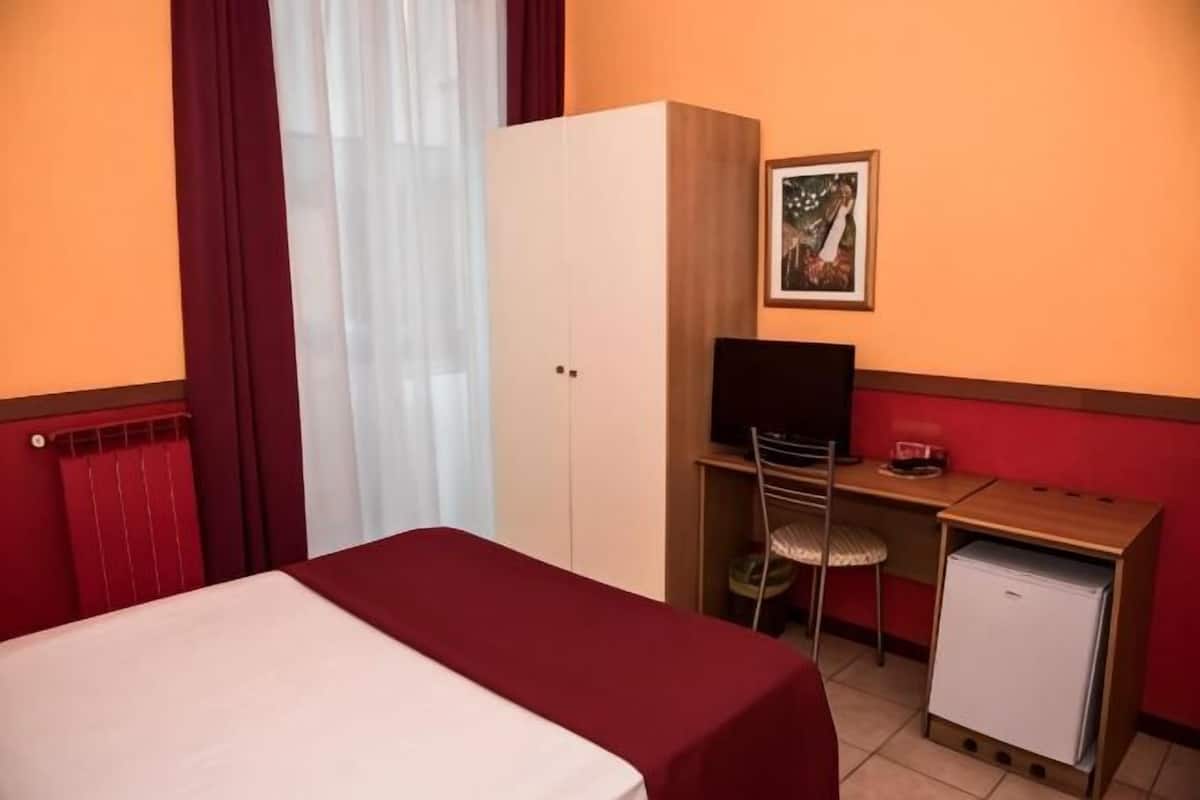A hotel room with a bed, a desk with a computer, a television, and a small refrigerator.