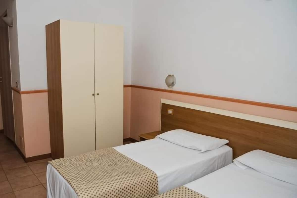 A room with two beds, a wardrobe, and a wall-mounted light fixture.