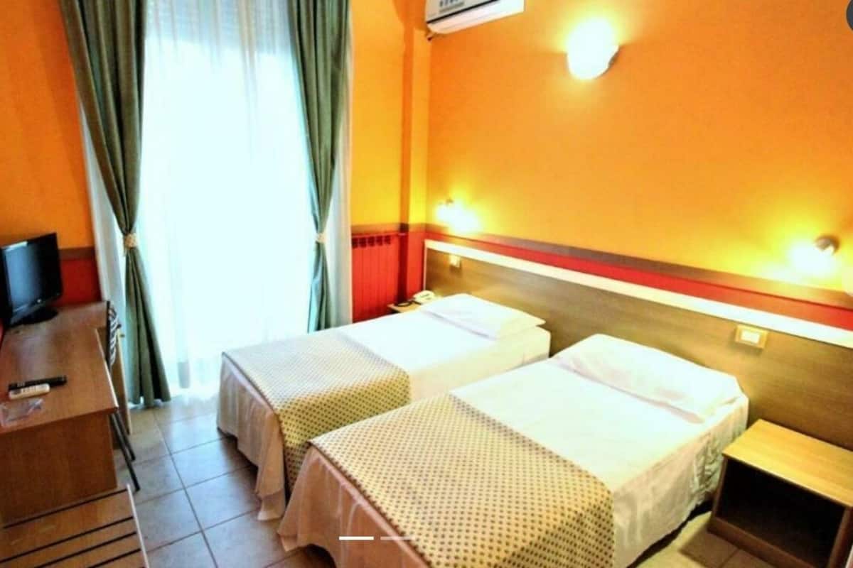A hotel room with two beds, a desk with a chair, a television, and a window with curtains.
